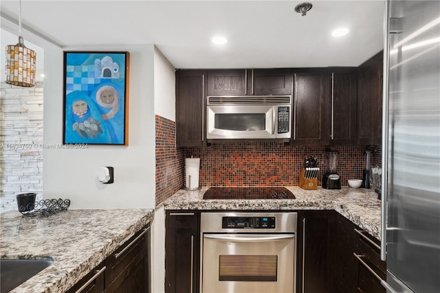 kitchen with dark brown cabinets, backsplash, light stone counters, stainless steel appliances, and decorative light fixtures