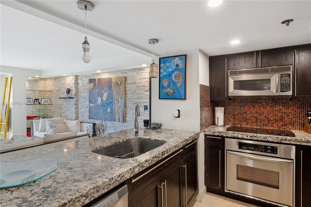 kitchen featuring appliances with stainless steel finishes, stone counters, sink, hanging light fixtures, and decorative backsplash