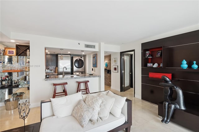 tiled living room featuring sink and stacked washer / dryer