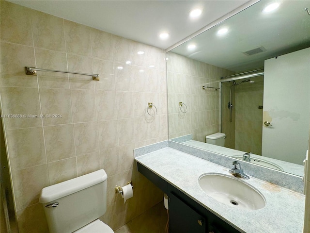 bathroom with vanity, toilet, a shower with shower door, and tile walls