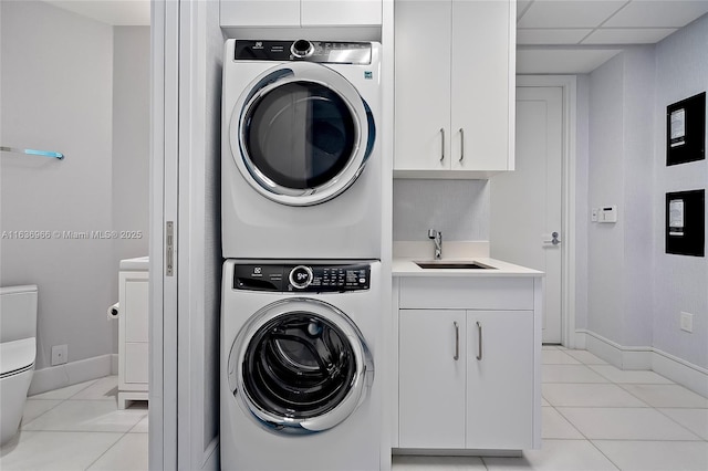 laundry room featuring stacked washer / drying machine, cabinet space, a sink, and light tile patterned floors