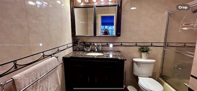 full bathroom featuring enclosed tub / shower combo, vanity, toilet, and tile walls