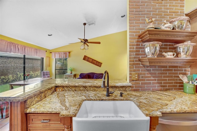 kitchen with kitchen peninsula, light stone counters, ceiling fan, sink, and lofted ceiling