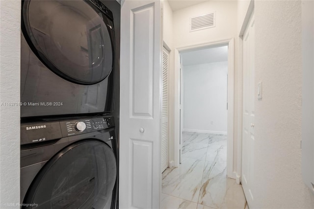 clothes washing area featuring light tile patterned floors and stacked washing maching and dryer