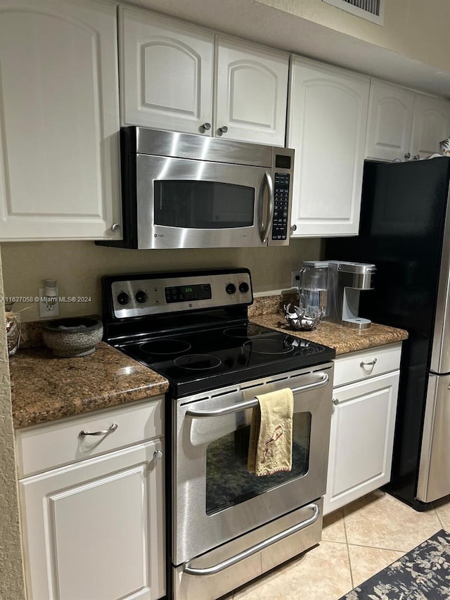 kitchen with dark stone counters, white cabinets, light tile patterned floors, and stainless steel appliances