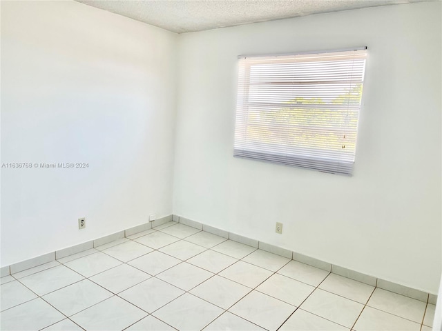 empty room with light tile patterned flooring, a textured ceiling, and plenty of natural light