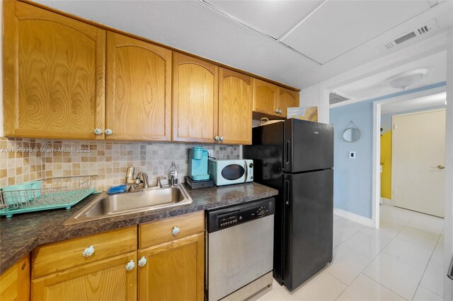 kitchen featuring dishwasher, sink, decorative backsplash, black refrigerator, and light tile patterned flooring