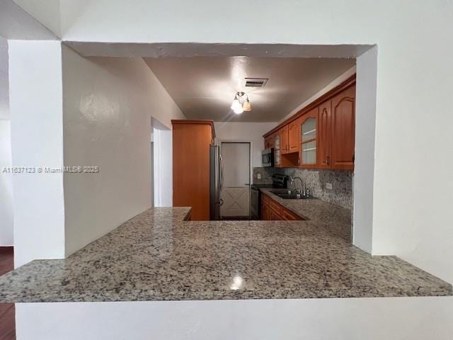 kitchen featuring visible vents, appliances with stainless steel finishes, light stone countertops, tasteful backsplash, and brown cabinetry