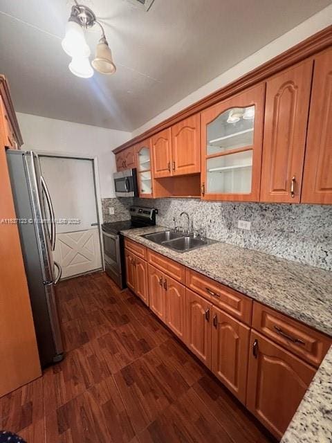 kitchen with a sink, appliances with stainless steel finishes, backsplash, dark wood finished floors, and glass insert cabinets