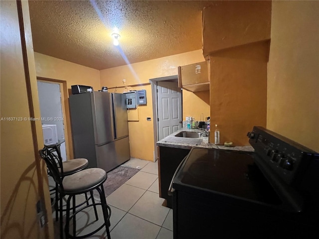 kitchen featuring a textured ceiling, sink, black electric range oven, light tile patterned flooring, and stainless steel fridge