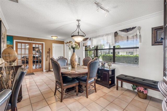 tiled dining room featuring rail lighting, ornamental molding, french doors, and a textured ceiling