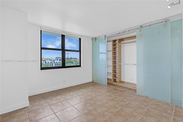 unfurnished bedroom with light tile patterned flooring, a barn door, and a closet