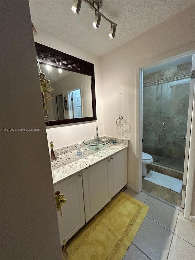 bathroom featuring toilet, a textured ceiling, a shower with door, tile patterned floors, and vanity