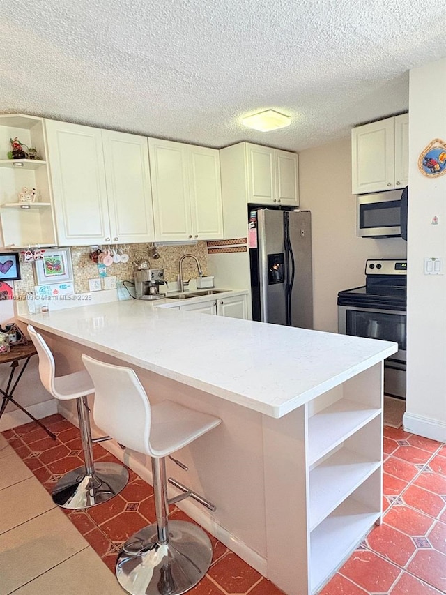 kitchen with a breakfast bar area, open shelves, a sink, a peninsula, and stainless steel appliances