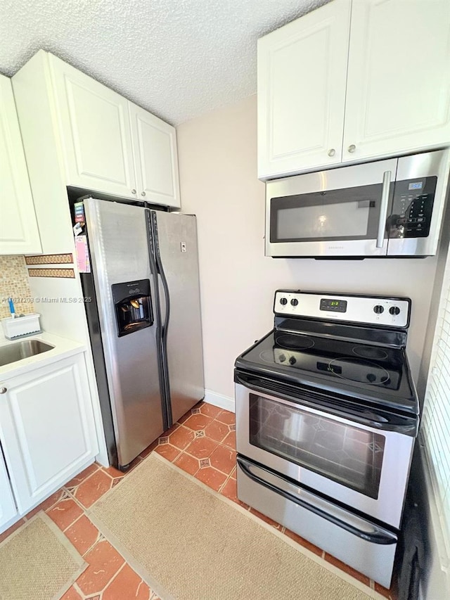 kitchen with a textured ceiling, appliances with stainless steel finishes, a sink, light countertops, and white cabinets