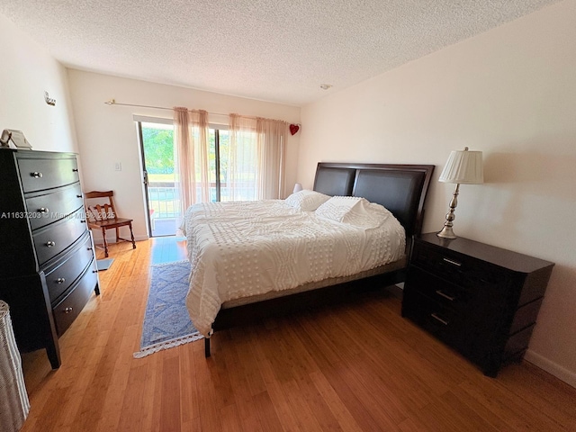 bedroom featuring access to outside, a textured ceiling, and wood finished floors