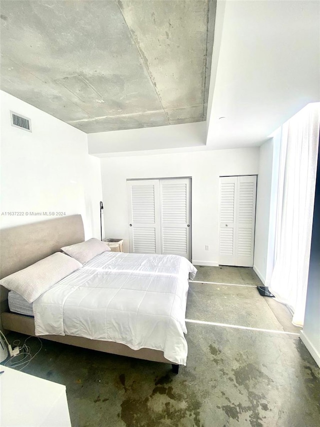 bedroom featuring concrete floors and two closets