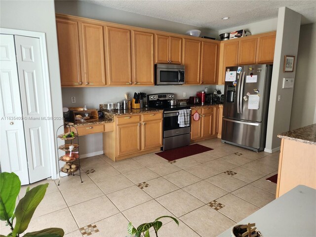 kitchen with light tile patterned flooring, dark stone counters, appliances with stainless steel finishes, and a textured ceiling