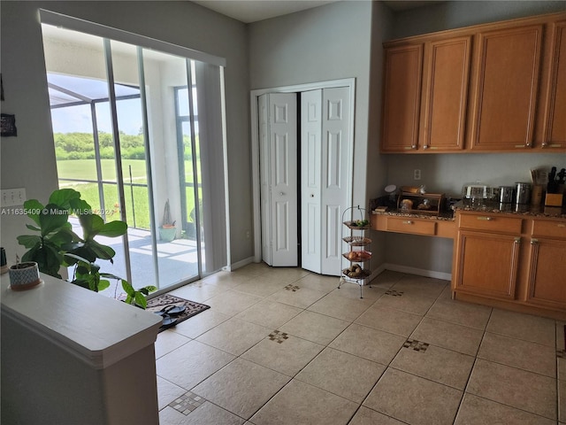 kitchen with light tile patterned flooring, dark stone counters, and built in desk