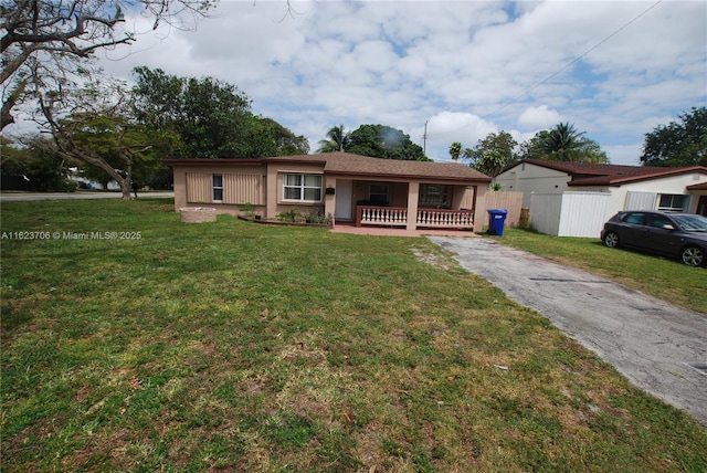 ranch-style home featuring aphalt driveway, covered porch, fence, a front lawn, and stucco siding