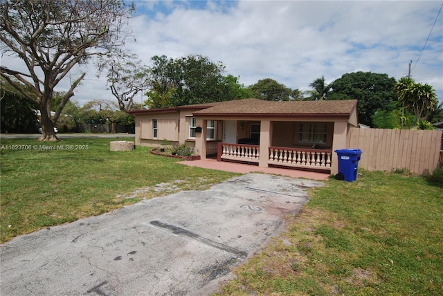 ranch-style house featuring covered porch, fence, and a front lawn