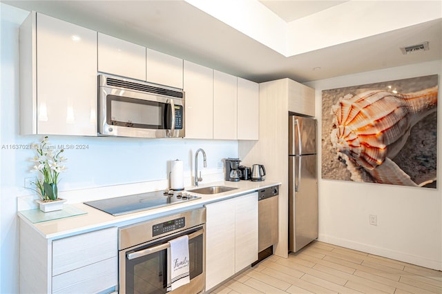 kitchen with white cabinets, light wood-type flooring, appliances with stainless steel finishes, and sink