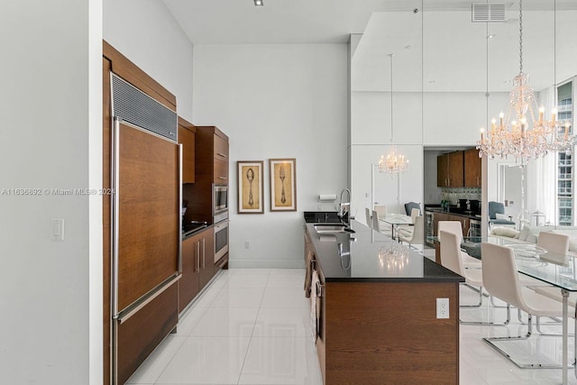 kitchen with built in appliances, a notable chandelier, an island with sink, and light tile patterned flooring