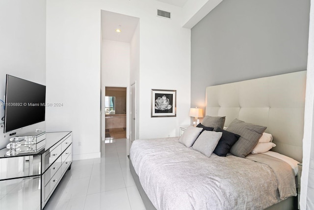 bedroom with light tile patterned floors, ensuite bathroom, and a towering ceiling