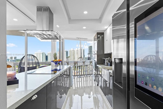 interior space with stainless steel fridge, light stone counters, a tray ceiling, island exhaust hood, and black electric cooktop