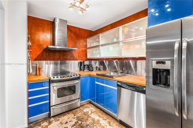 kitchen with tasteful backsplash, wall chimney range hood, wood counters, stainless steel appliances, and sink