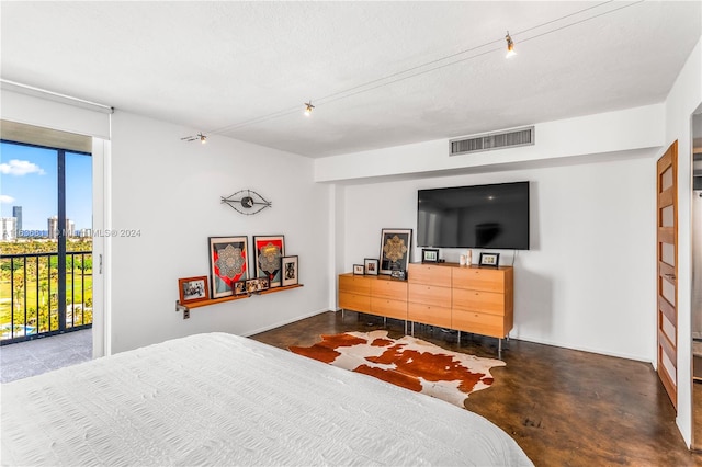 bedroom featuring access to exterior, rail lighting, a textured ceiling, and concrete floors