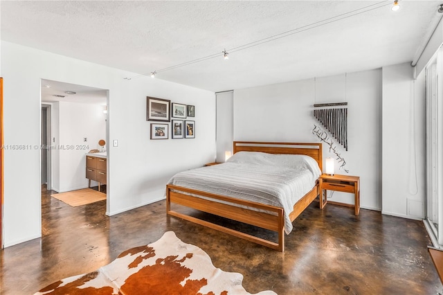 bedroom with a textured ceiling, connected bathroom, and track lighting