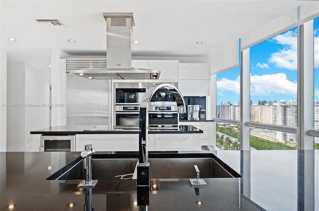 kitchen with island range hood, white cabinets, plenty of natural light, and wine cooler