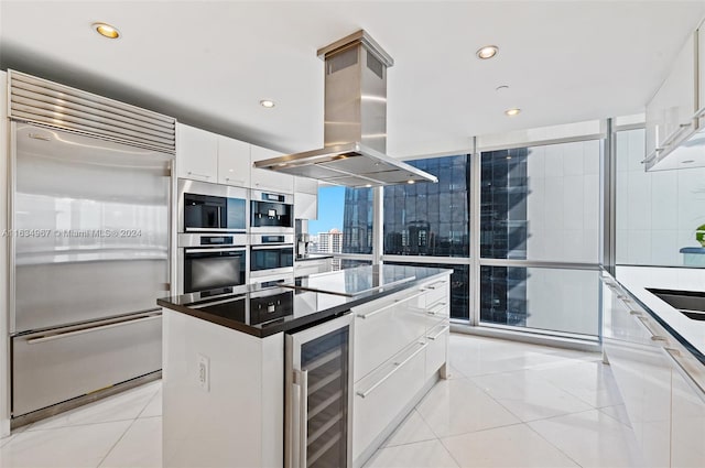 kitchen featuring beverage cooler, appliances with stainless steel finishes, island range hood, white cabinetry, and a center island