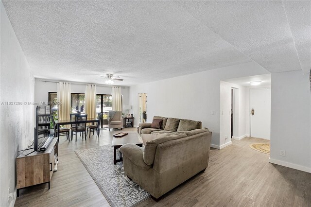 living room with ceiling fan, light wood-type flooring, and a textured ceiling