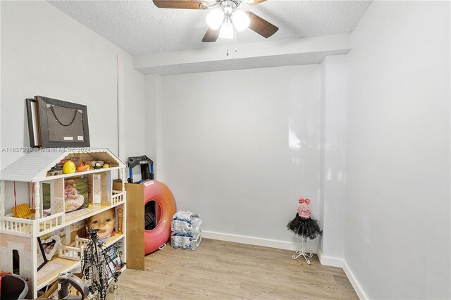 game room with a textured ceiling, ceiling fan, and light wood-type flooring