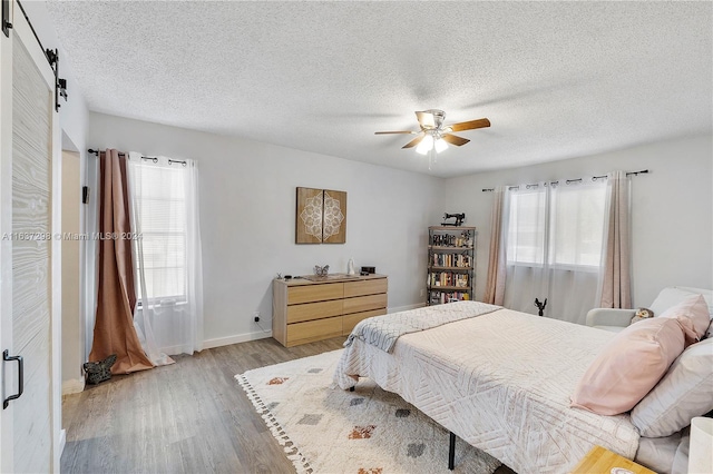 bedroom featuring a barn door, a textured ceiling, ceiling fan, and light wood-type flooring