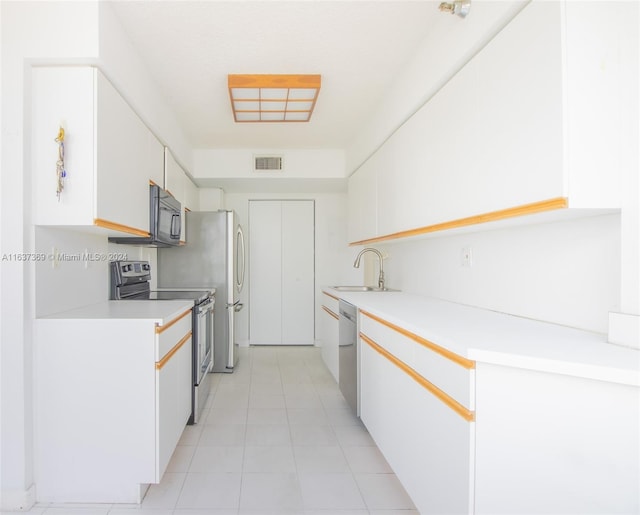 kitchen with appliances with stainless steel finishes, white cabinetry, light tile patterned floors, and sink