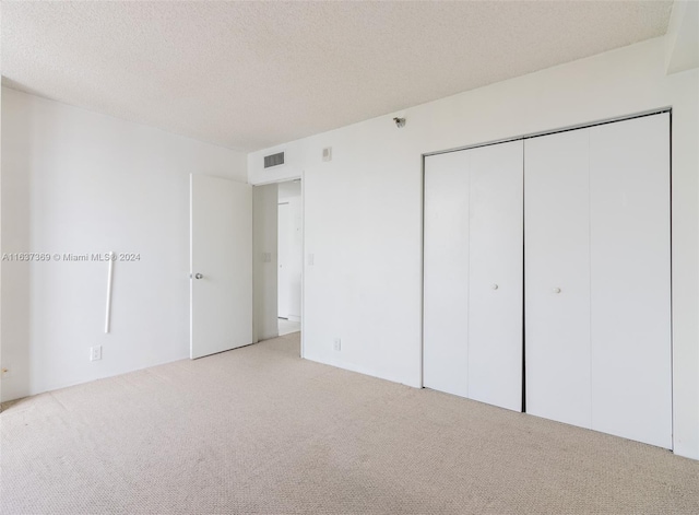 unfurnished bedroom featuring light carpet, a closet, and a textured ceiling