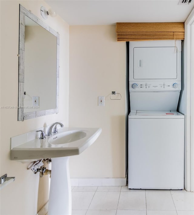 laundry area featuring light tile patterned flooring, stacked washer and clothes dryer, and sink