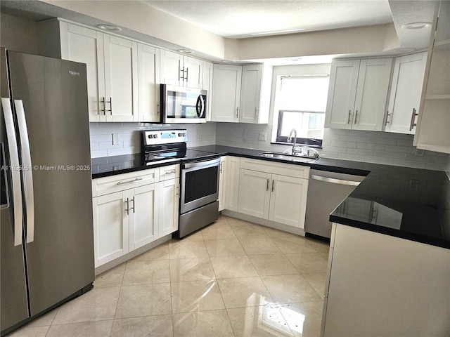 kitchen with appliances with stainless steel finishes, white cabinetry, decorative backsplash, sink, and light tile patterned floors