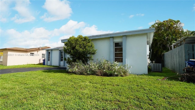 view of front of property with cooling unit, fence, a front lawn, and stucco siding