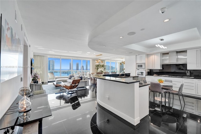 kitchen with white appliances, dark countertops, wall chimney exhaust hood, a healthy amount of sunlight, and white cabinetry