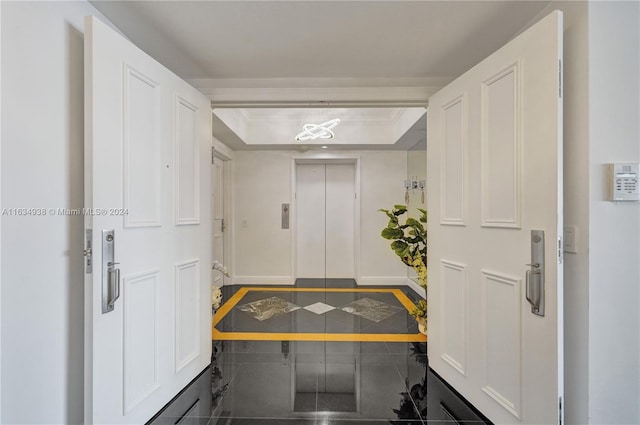 foyer entrance with crown molding, a tray ceiling, baseboards, and elevator