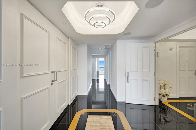 hall with a notable chandelier, a tray ceiling, and crown molding