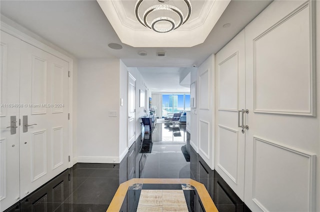 hall featuring dark tile patterned floors, ornamental molding, and a tray ceiling