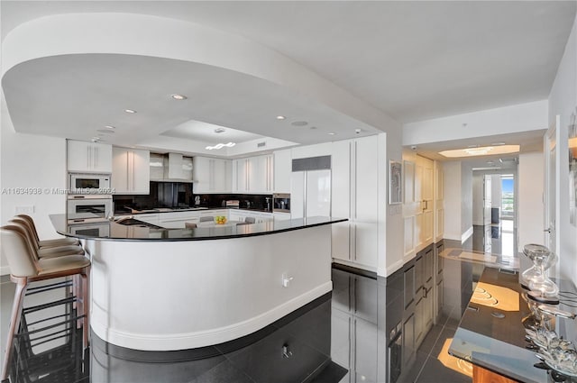 kitchen with dark tile patterned flooring, built in appliances, white cabinetry, decorative backsplash, and a kitchen island