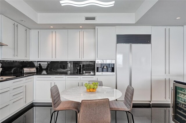 kitchen featuring a raised ceiling, wine cooler, backsplash, paneled built in refrigerator, and white cabinets