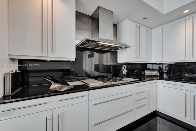 kitchen with gas cooktop, white cabinets, backsplash, dark tile patterned floors, and wall chimney exhaust hood