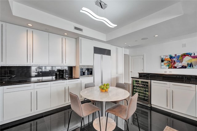 kitchen featuring a raised ceiling, wine cooler, pendant lighting, paneled refrigerator, and white cabinets